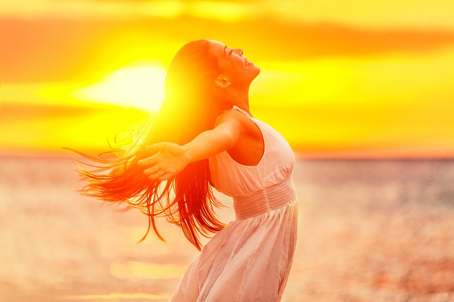 Happy woman feeling free with open arms in sunshine at beach sun